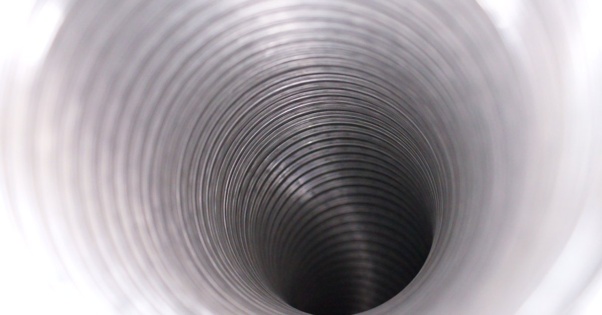 An up-close view of the inside of an aluminum air duct. The duct has ridges throughout and curves downward.